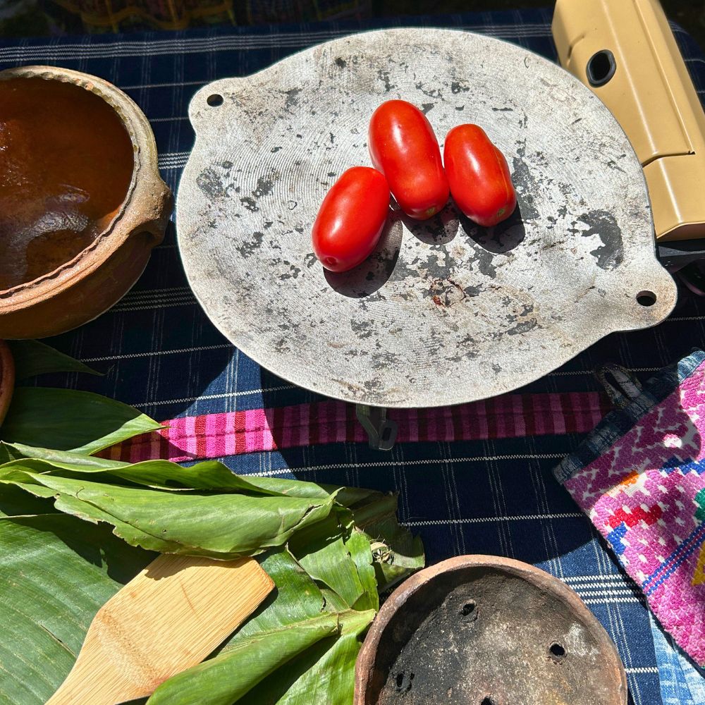 A traditional steel comal with fresh red tomatoes roasting over heat to prepare chilmol, a traditional Guatemalan tomato sauce.