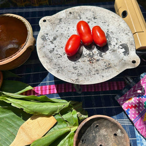A traditional steel comal with fresh red tomatoes roasting over heat to prepare chilmol, a traditional Guatemalan tomato sauce.
