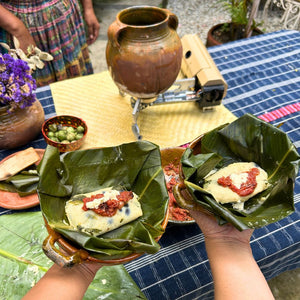 Two freshly steamed corn masa tamales served with traditional Guatemalan chilmol and queso de monte, a regional artisanal cheese.