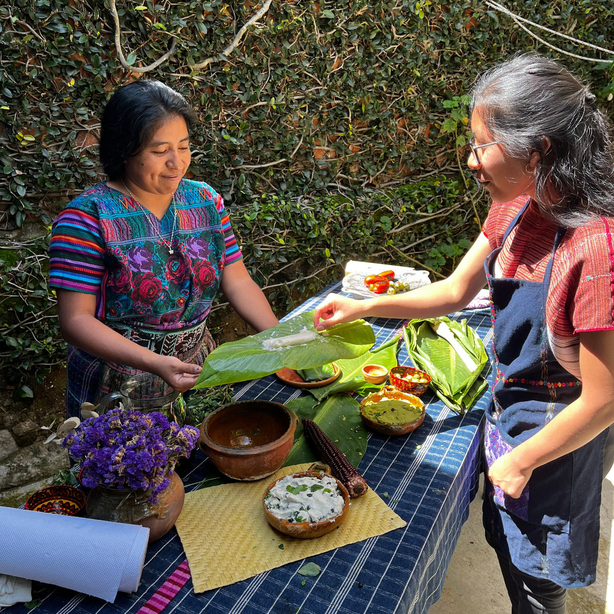 Two women preparing food outdoors with a table set.