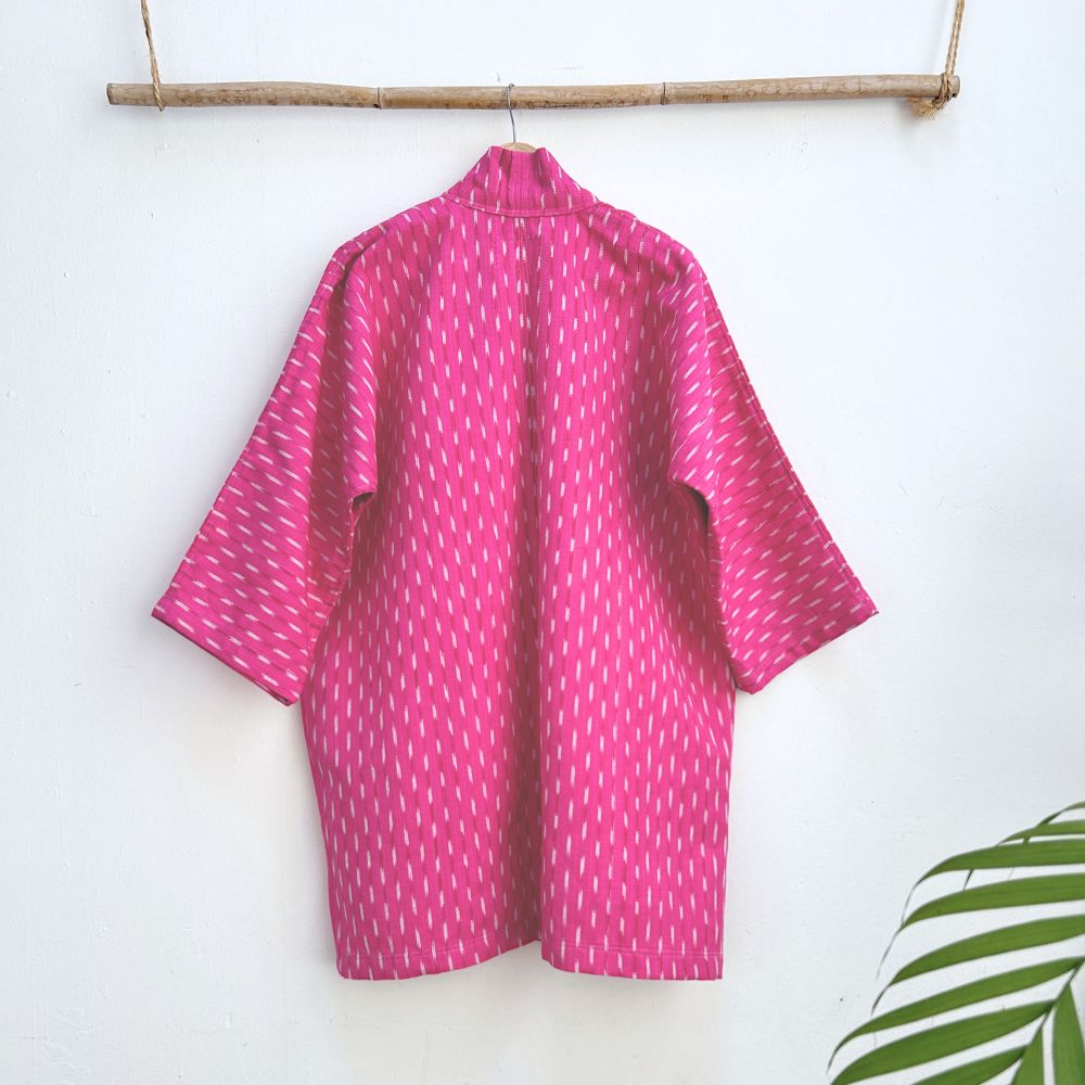 Pink patterned jacket hanging on a wooden rod against a white wall.