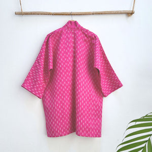 Pink patterned jacket hanging on a wooden rod against a white wall.