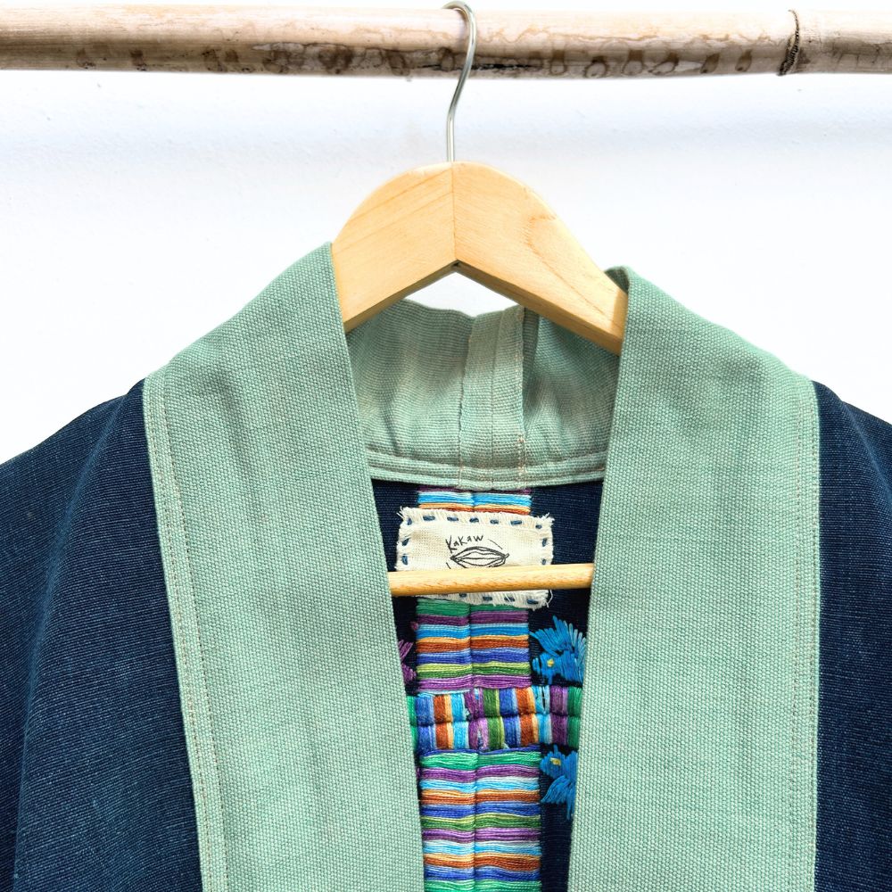 Green jacket neck with colorful embroidered fabric underneath on a wooden hanger against a white background