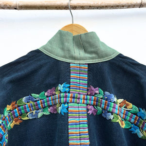 Navy blue jacket with colorful embroidery on a hanger against a white background