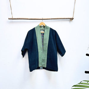 Navy blue and green jacket on a hanger against a white wall