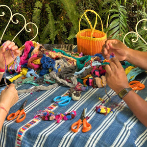 A table in the garden filled with vibrant colorful threads, scissors, and hands preparing the base to create traditional Chajul-style pom poms.