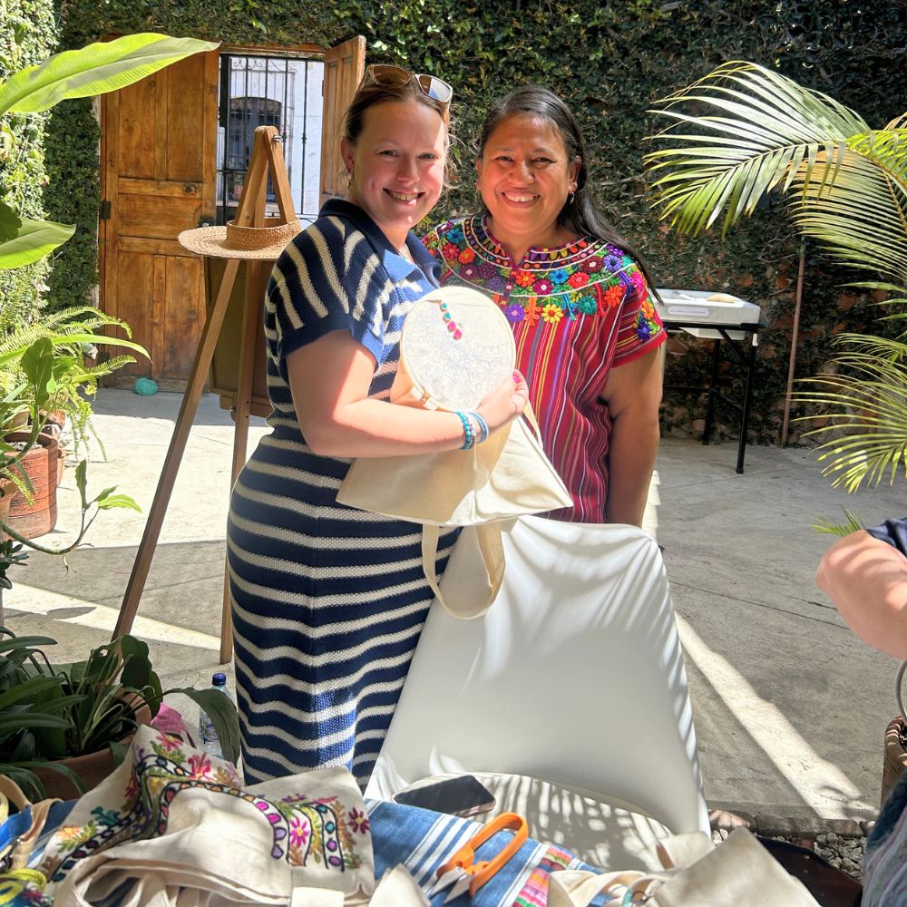 A teacher and her student smiling while showing some of the embroidery stitches learned during the class.