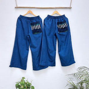 Pair of blue pants with striped pockets on hangers against a white background