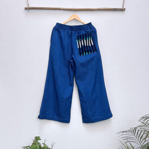 Blue pants with a patch pocket on a hanger against a white wall.