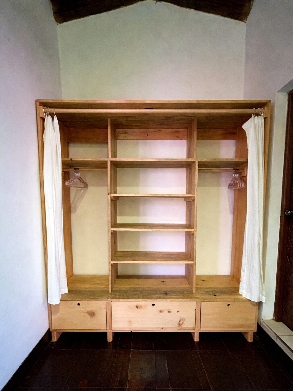 Wooden wardrobe with shelves and hanging rods in a room.