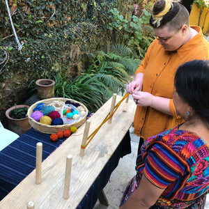 Two people working on a warping board outdoors with colorful thread.
