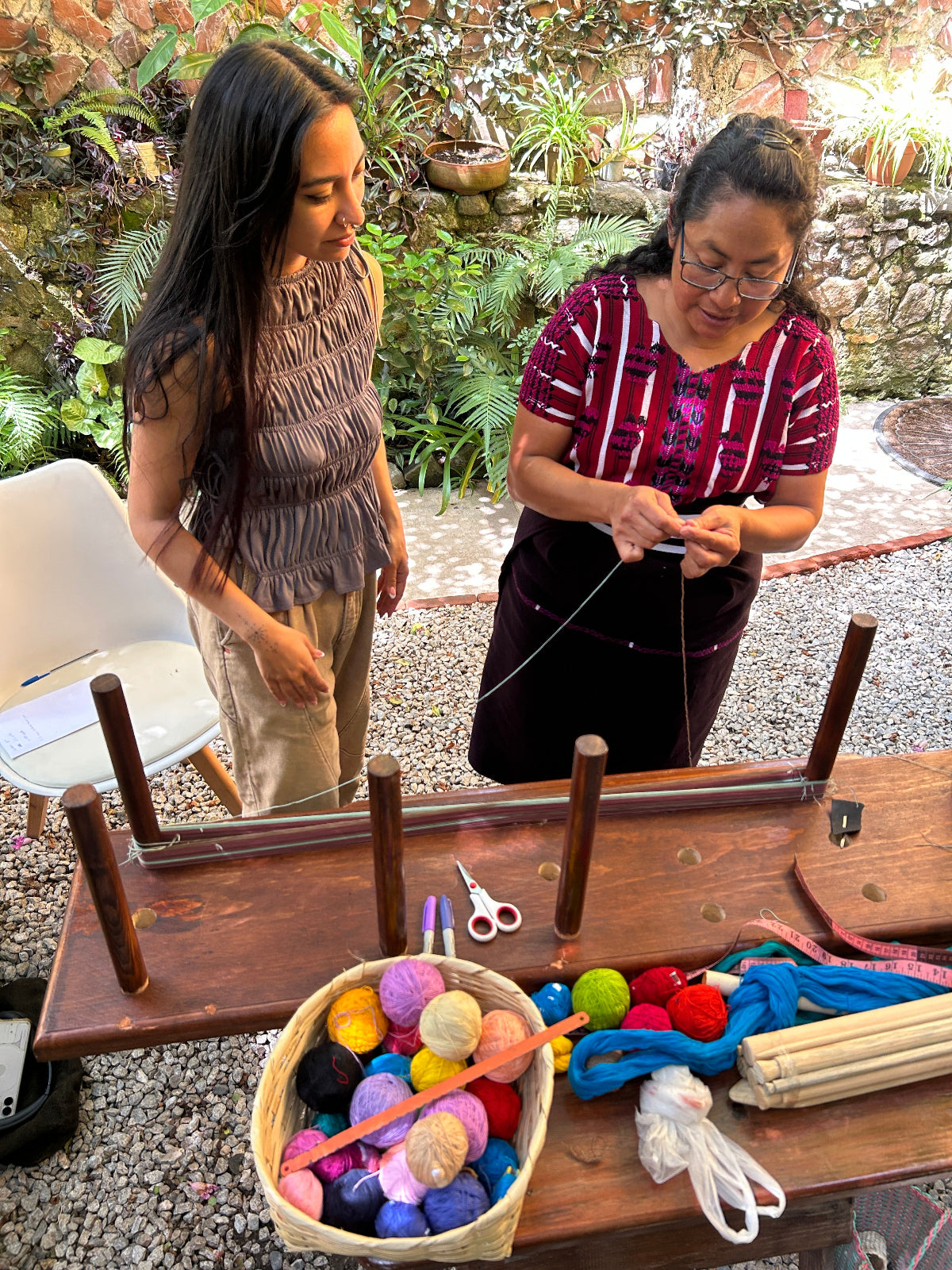 Two women working with thread on a warping board outdoors.