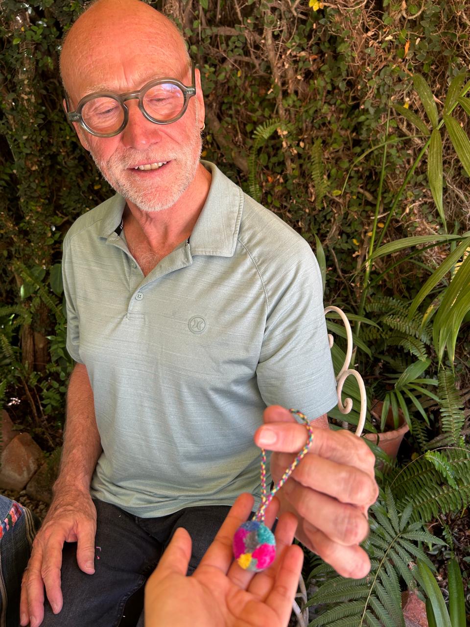 Our friend Andrew holding the pompom he made himself during the class. He is smiling broadly and proudly displaying his pompom, which features vibrant colors.