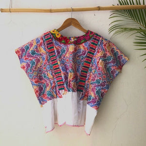 Colorful woven huipil on a hanger against a light background