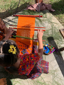 A young weaver showing off her brocade skills on a vibrant backstrap loom.