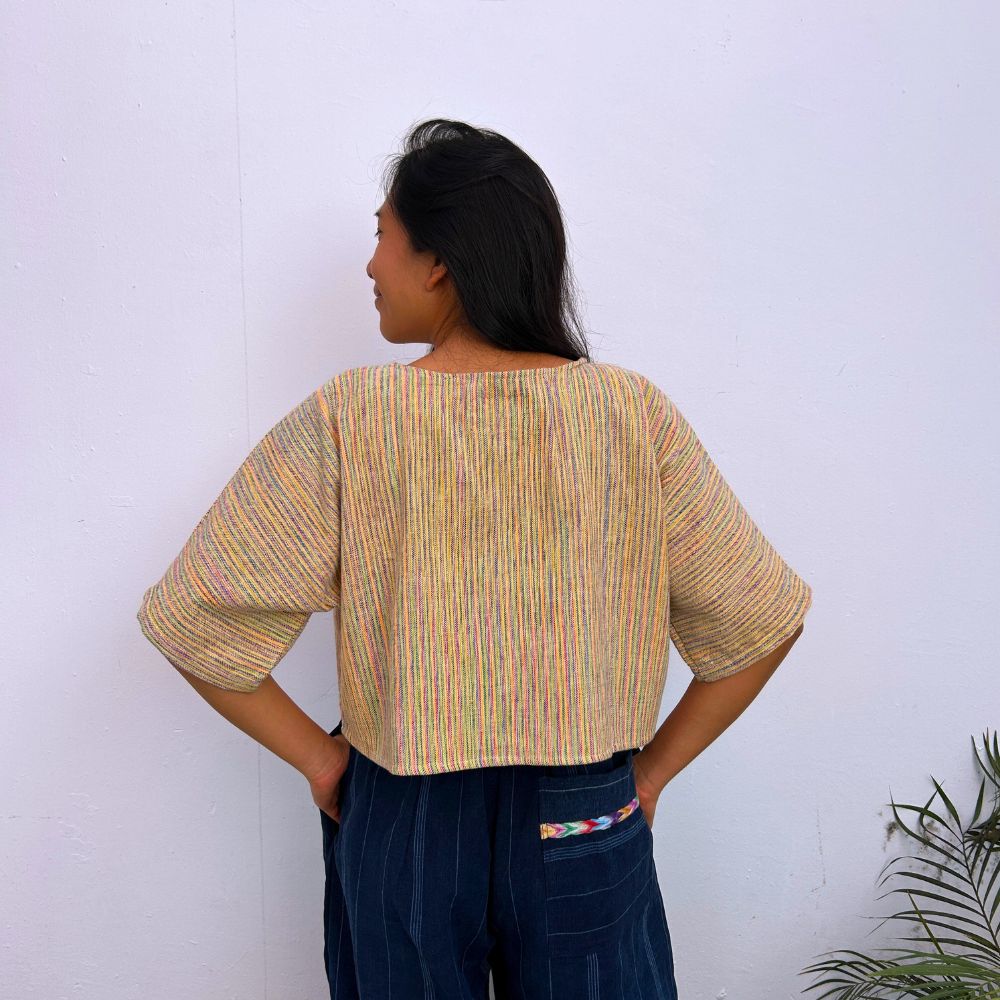 Model wearing a colorful striped top and dark pants against a white wall