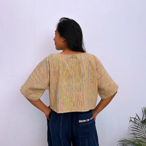 Model wearing a colorful striped top and dark pants against a white wall
