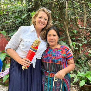 Two women standing together outdoors with one holding a colorful loom.