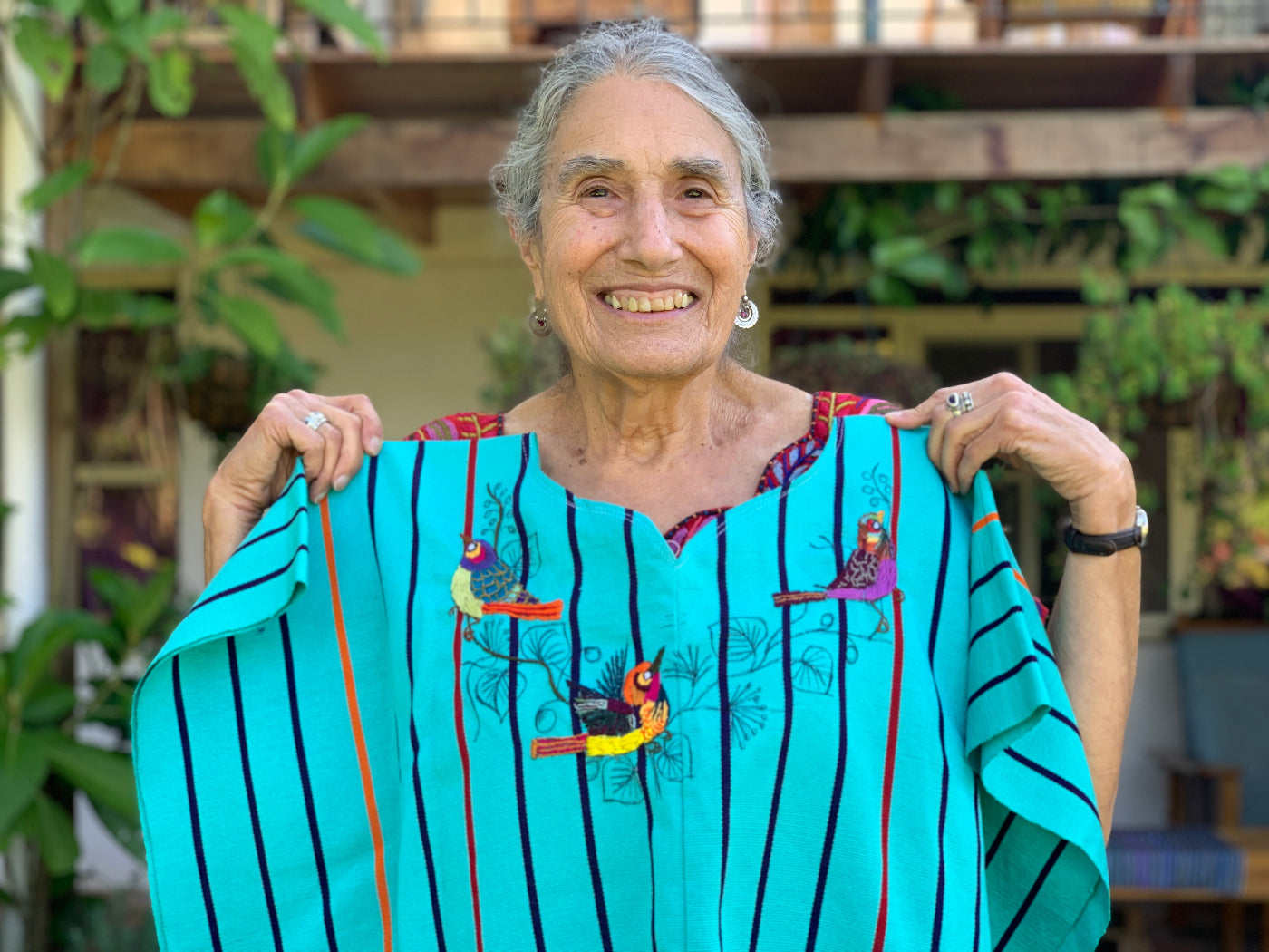 Woman holding a colorful garment with embroidery, standing outdoors.