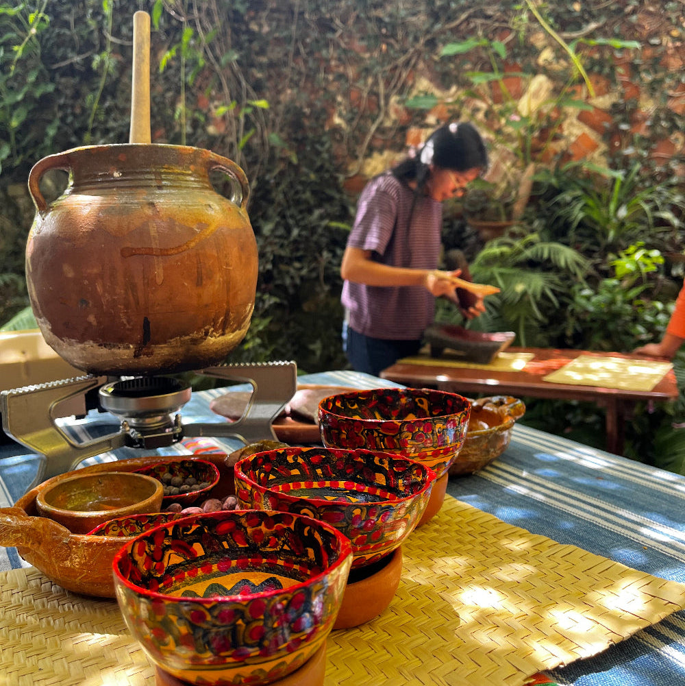 Traditional clay and hand-painted gourd vessels for cacao in a lush garden