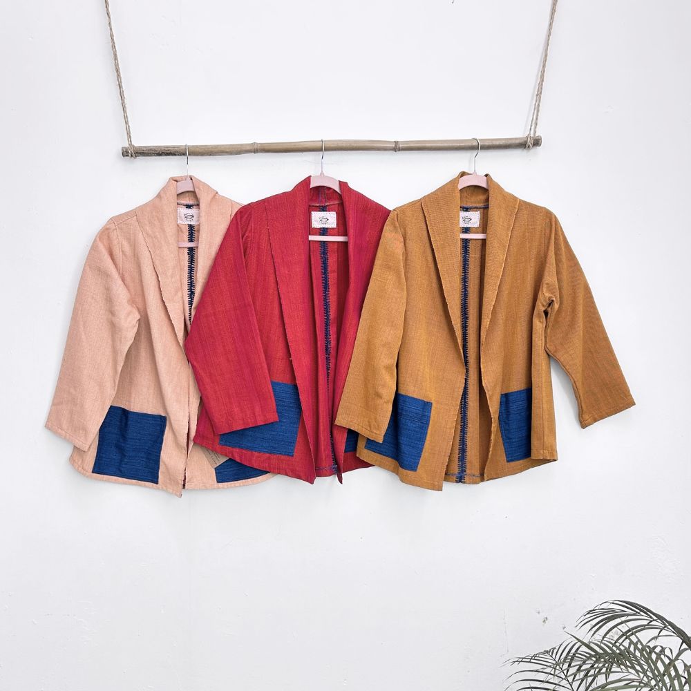 Three jackets in beige, red, and mustard with blue front pockets hanging on a rack against a white background.