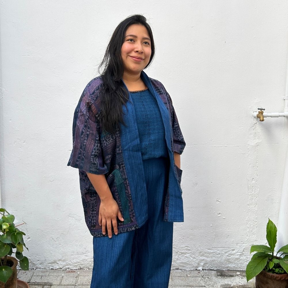 Woman wearing a blue outfit with a patterned jacket against a white wall.