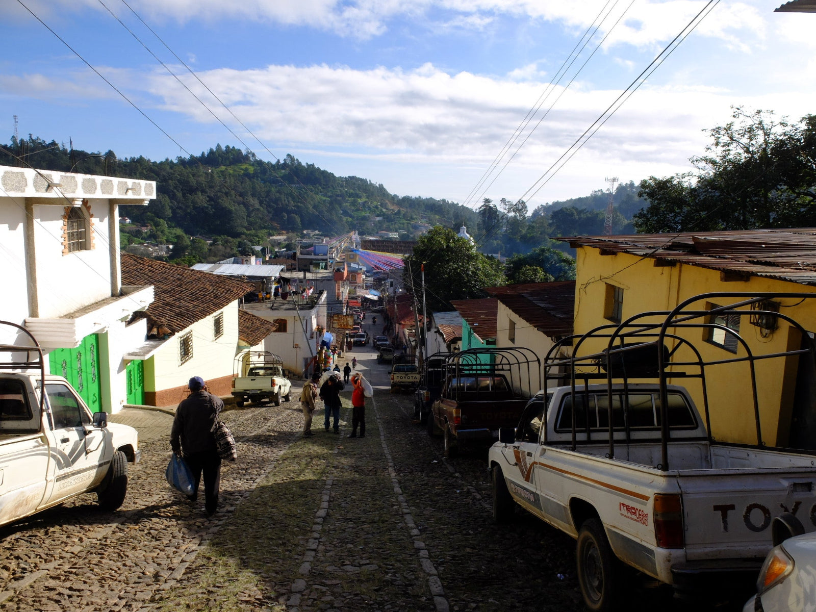 Street scene in a small town with vehicles and people on a sunny day.