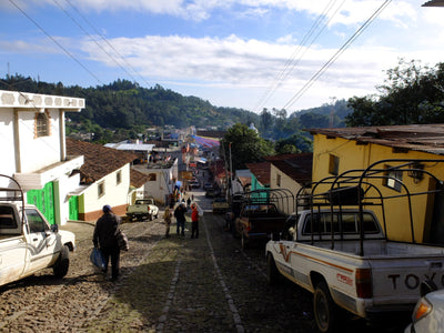 Street scene in a small town with vehicles and people on a sunny day.