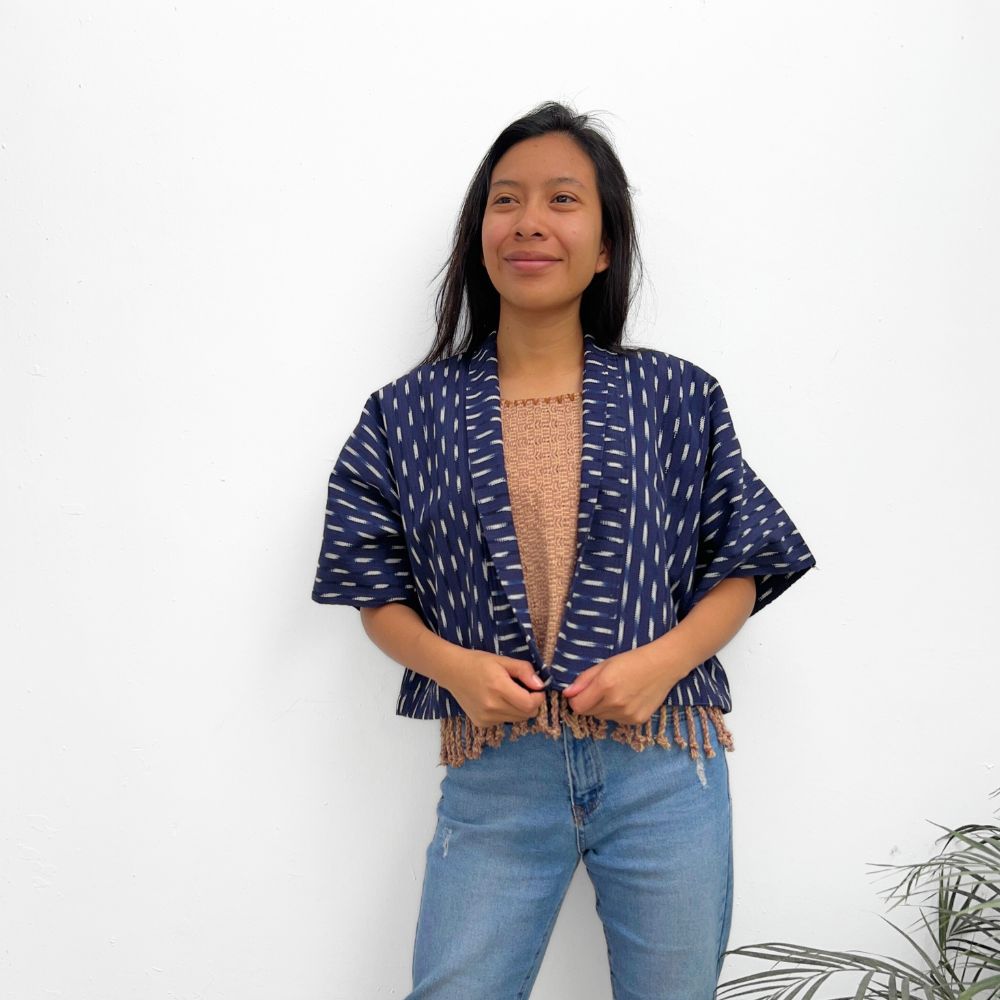 A woman wearing an Indigo blue jacket with a white ikat pattern, paired with a beige top and blue jeans.