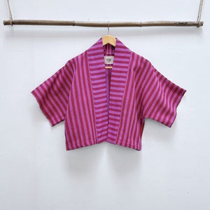  Two Shades of pink striped cropped jacket hanging on a wooden hanger against a white background.