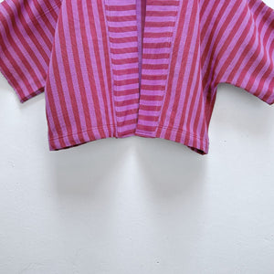 Close-up of Two Shades of pink striped cropped jacket hanging on a wooden hanger against a white background.
