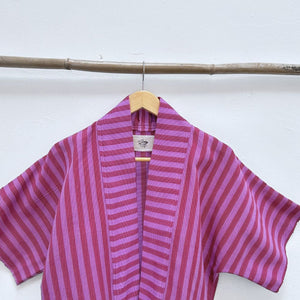 Two Shades of pink striped cropped jacket hanging on a wooden hanger against a white background.