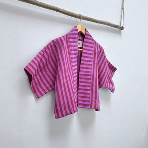 Two Shades of pink striped cropped jacket hanging on a wooden hanger against a white background.